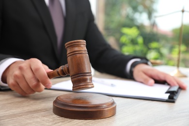 Photo of Judge with gavel at wooden table indoors, closeup. Criminal law