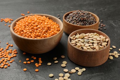 Different types of lentils in bowls on grey textured table