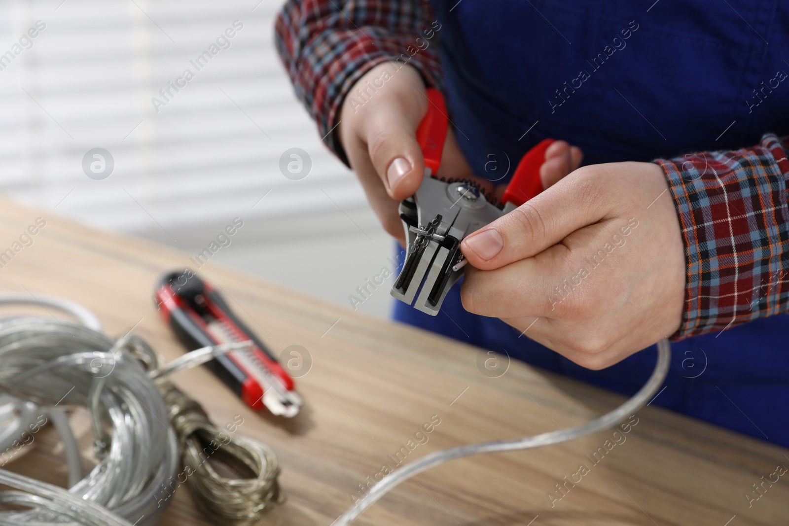 Photo of Professional electrician stripping wiring at wooden table, closeup view