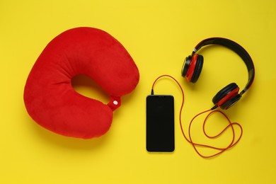 Photo of Red travel pillow, smartphone and headphones on yellow background, flat lay