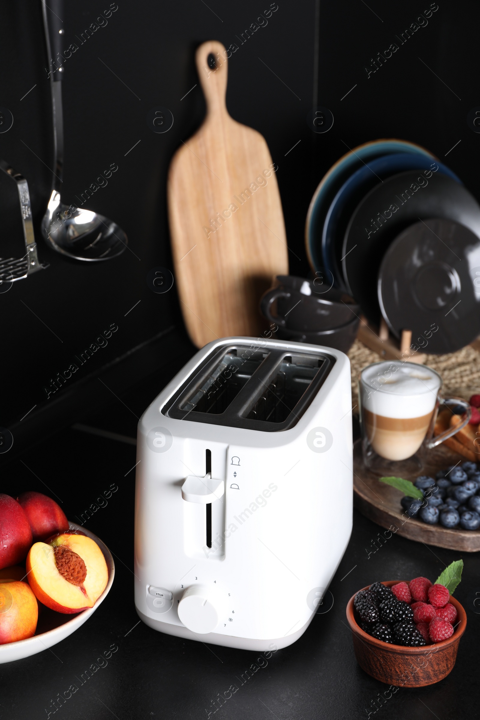 Photo of Modern toaster, fresh berries and coffee on black table