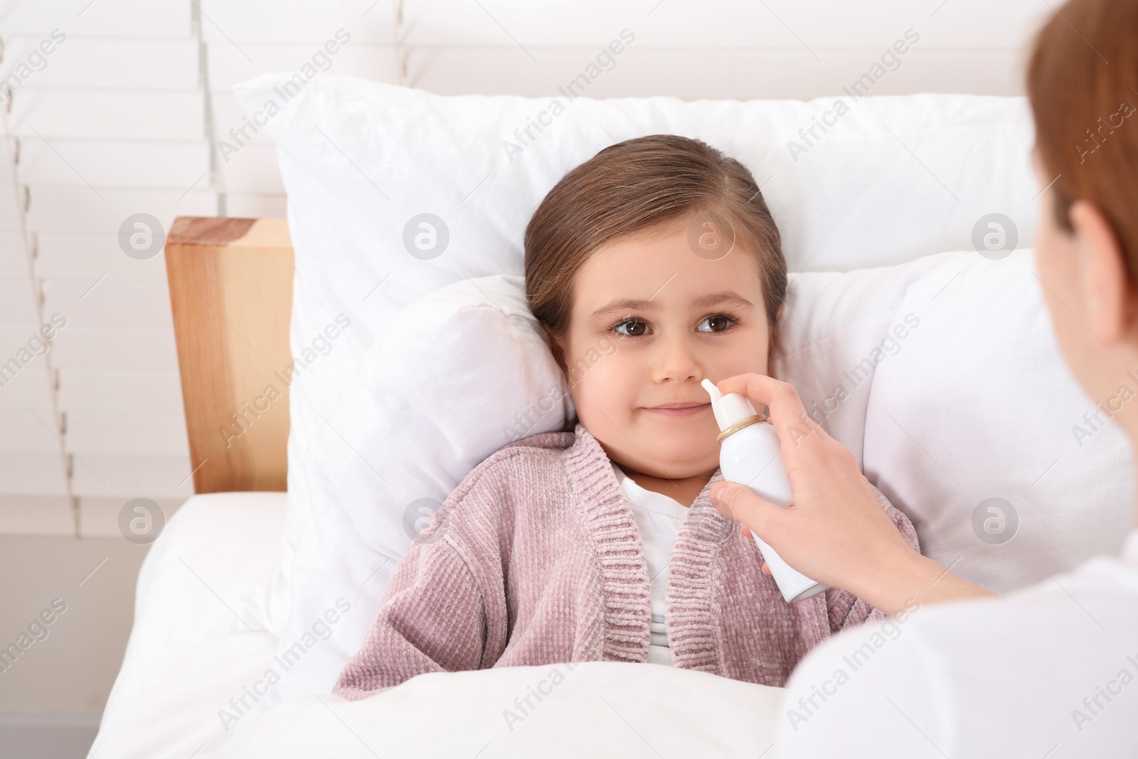 Photo of Mother using nasal spray to treat her little daughter on bed