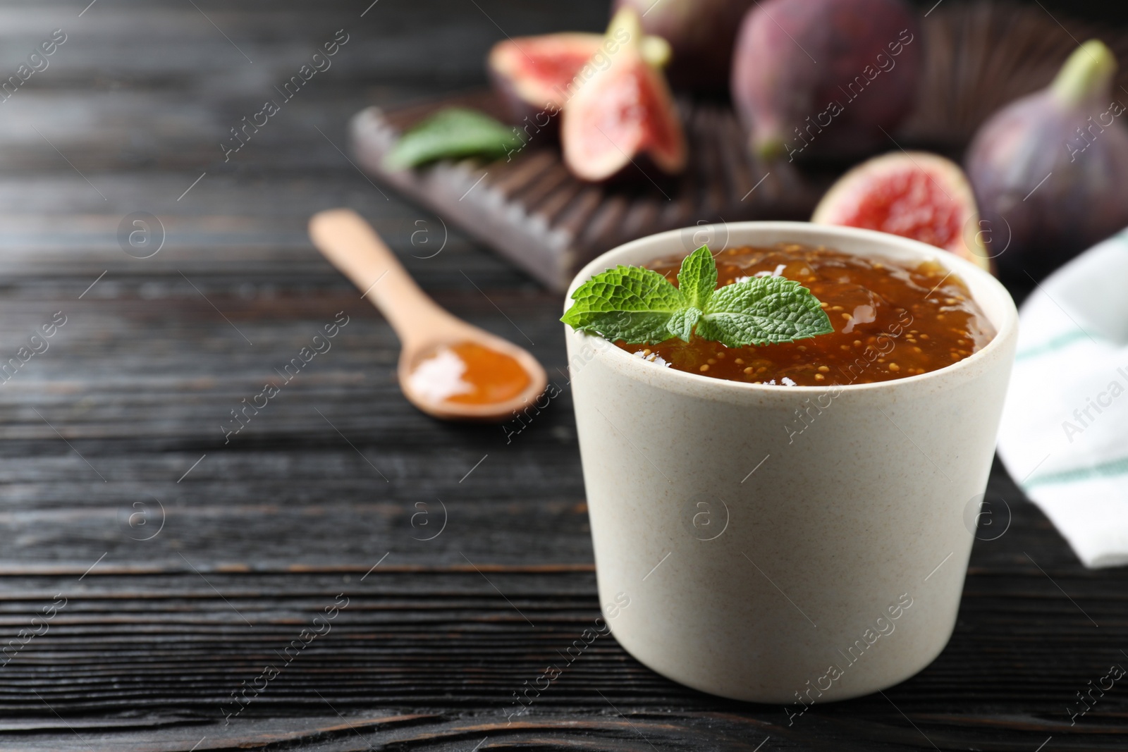 Photo of Homemade delicious fig jam with mint on black wooden table. Space for text