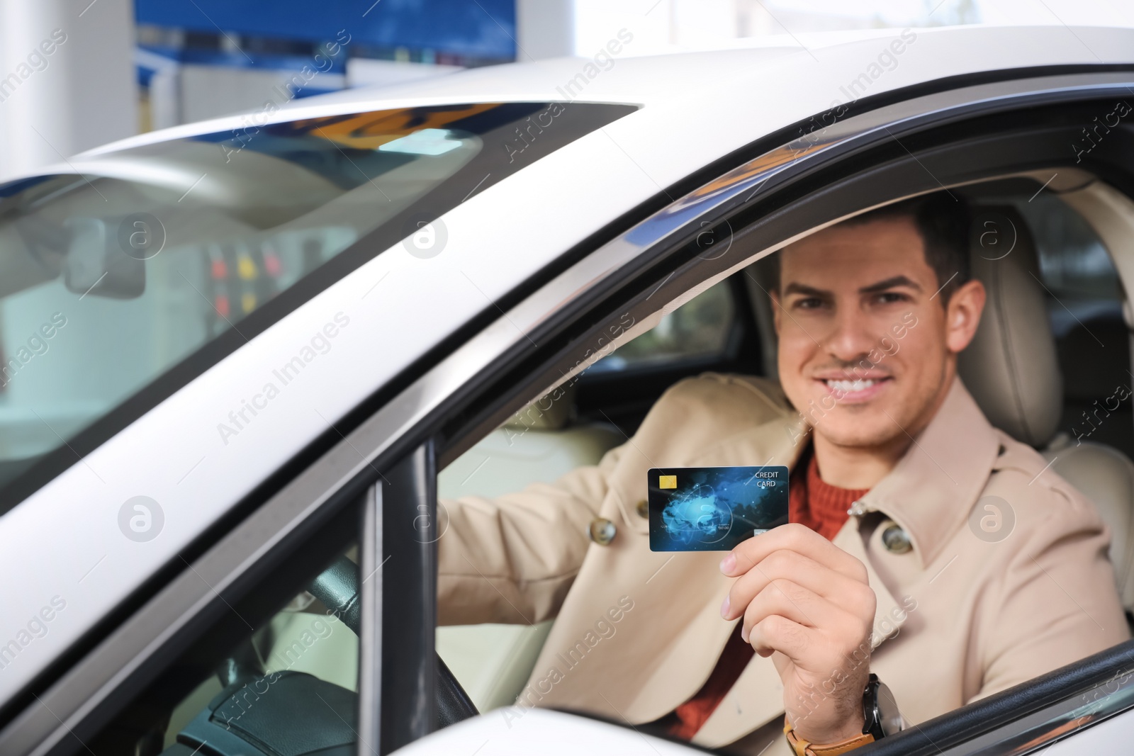 Photo of Man sitting in car and showing credit card at gas station, focus on hand