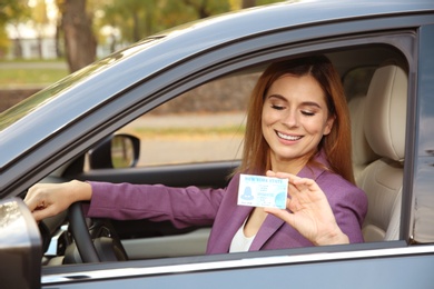 Happy woman holding driving license in car