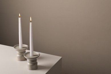Holders with burning candles on white table near pale brown wall, space for text