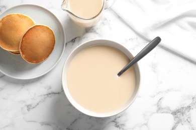 Photo of Bowl of condensed milk and pancakes served on marble table, top view. Dairy products