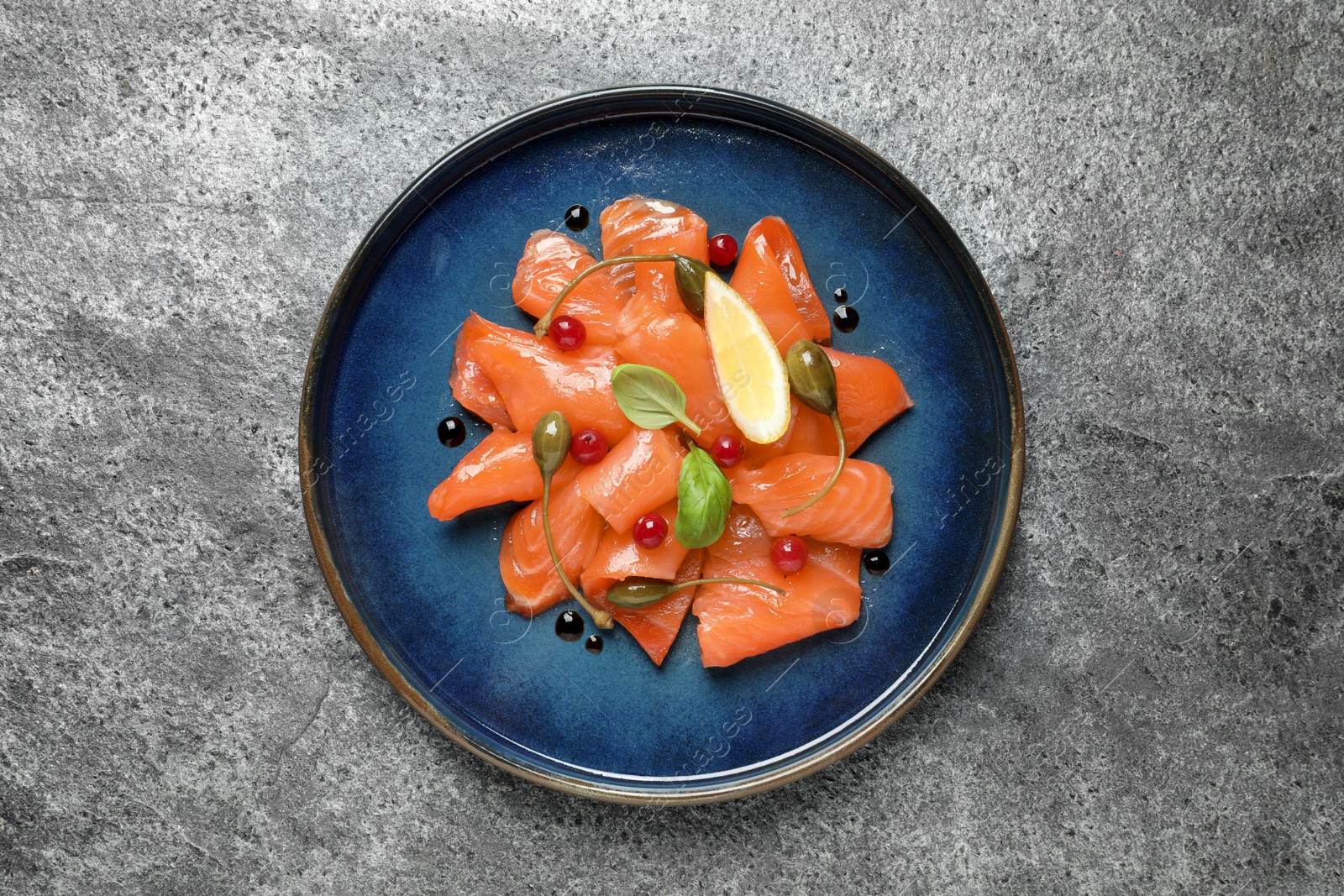 Photo of Salmon carpaccio with capers, cranberries, basil and lemon on grey table, top view