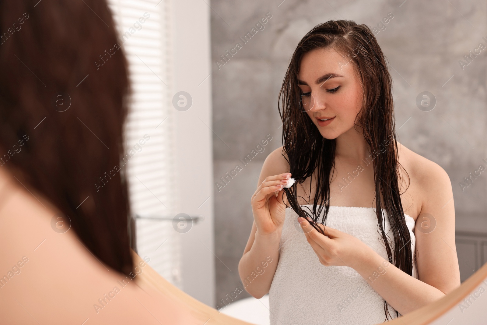 Photo of Young woman applying hair mask near mirror in bathroom