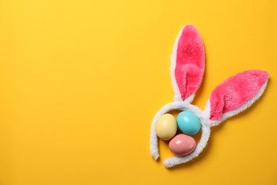 Funny headband with Easter bunny ears and dyed eggs on color background, flat lay. Space for text