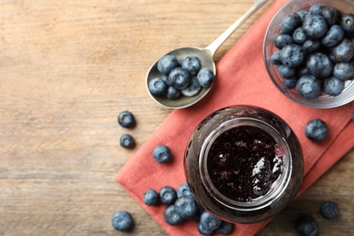 Photo of Jar of blueberry jam and fresh berries on wooden table, top view. Space for text