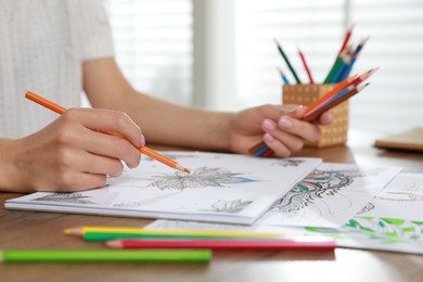 Photo of Young woman coloring antistress page at table indoors, closeup