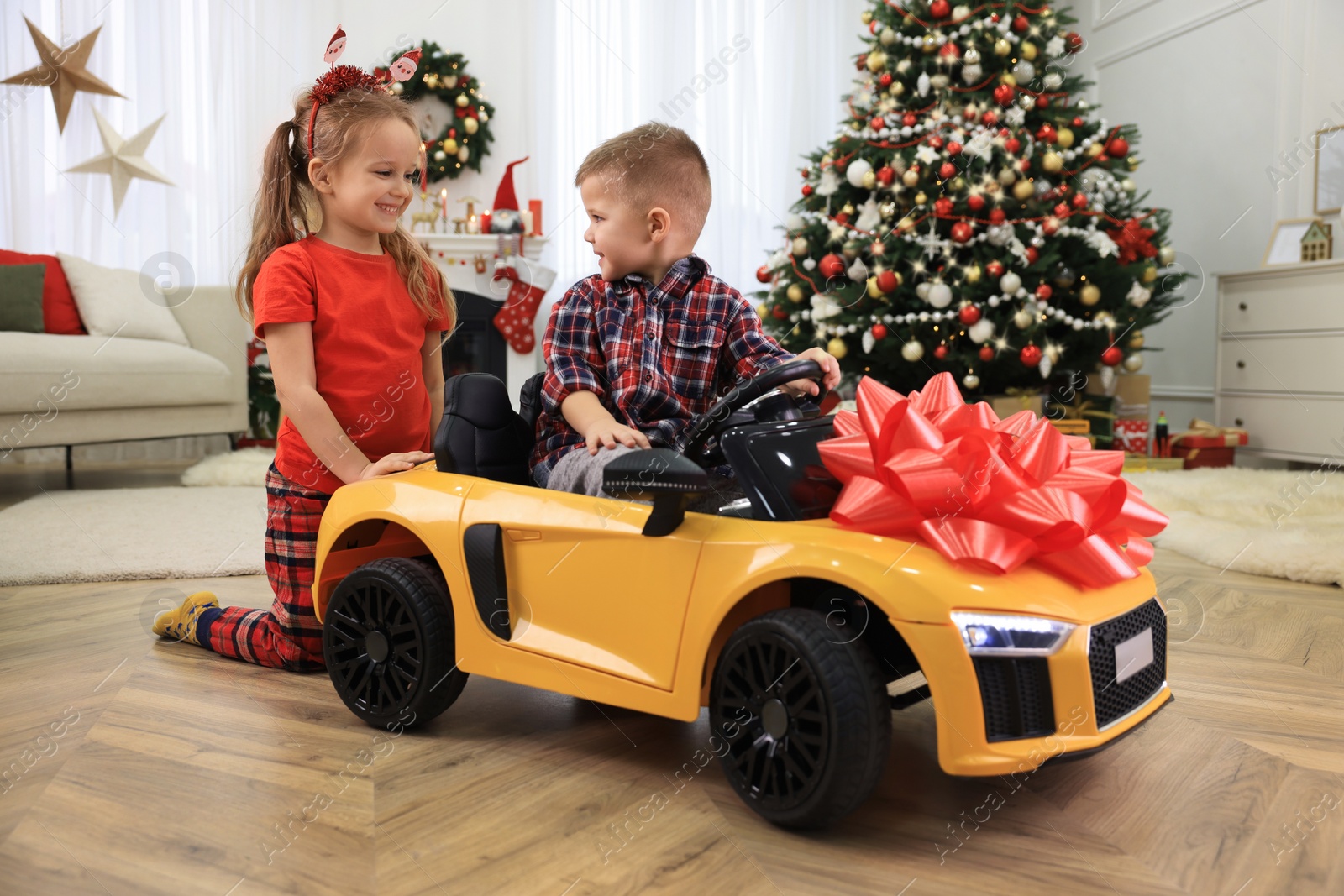 Photo of Cute little children playing with toy car in room decorated for Christmas