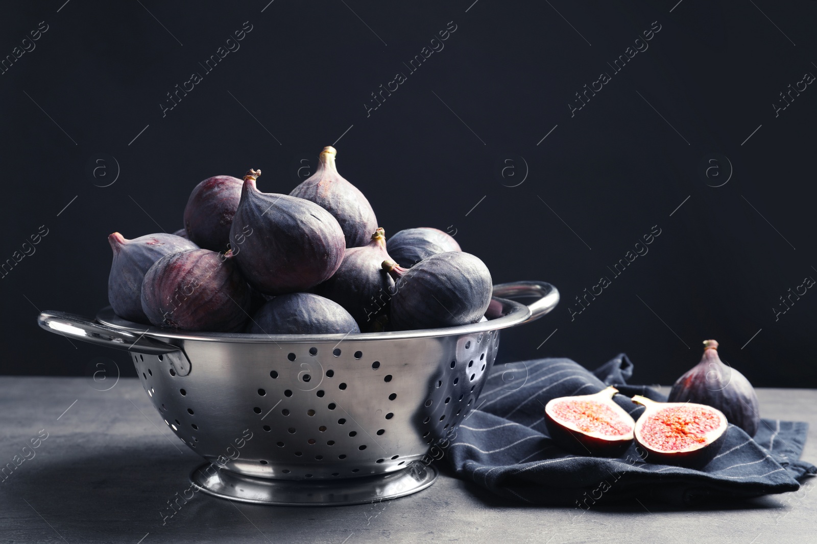 Photo of Colander with fresh ripe figs on table against black background