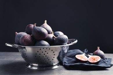 Colander with fresh ripe figs on table against black background