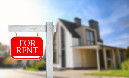 Image of Sign with phrase FOR RENT and blurred view of beautiful house