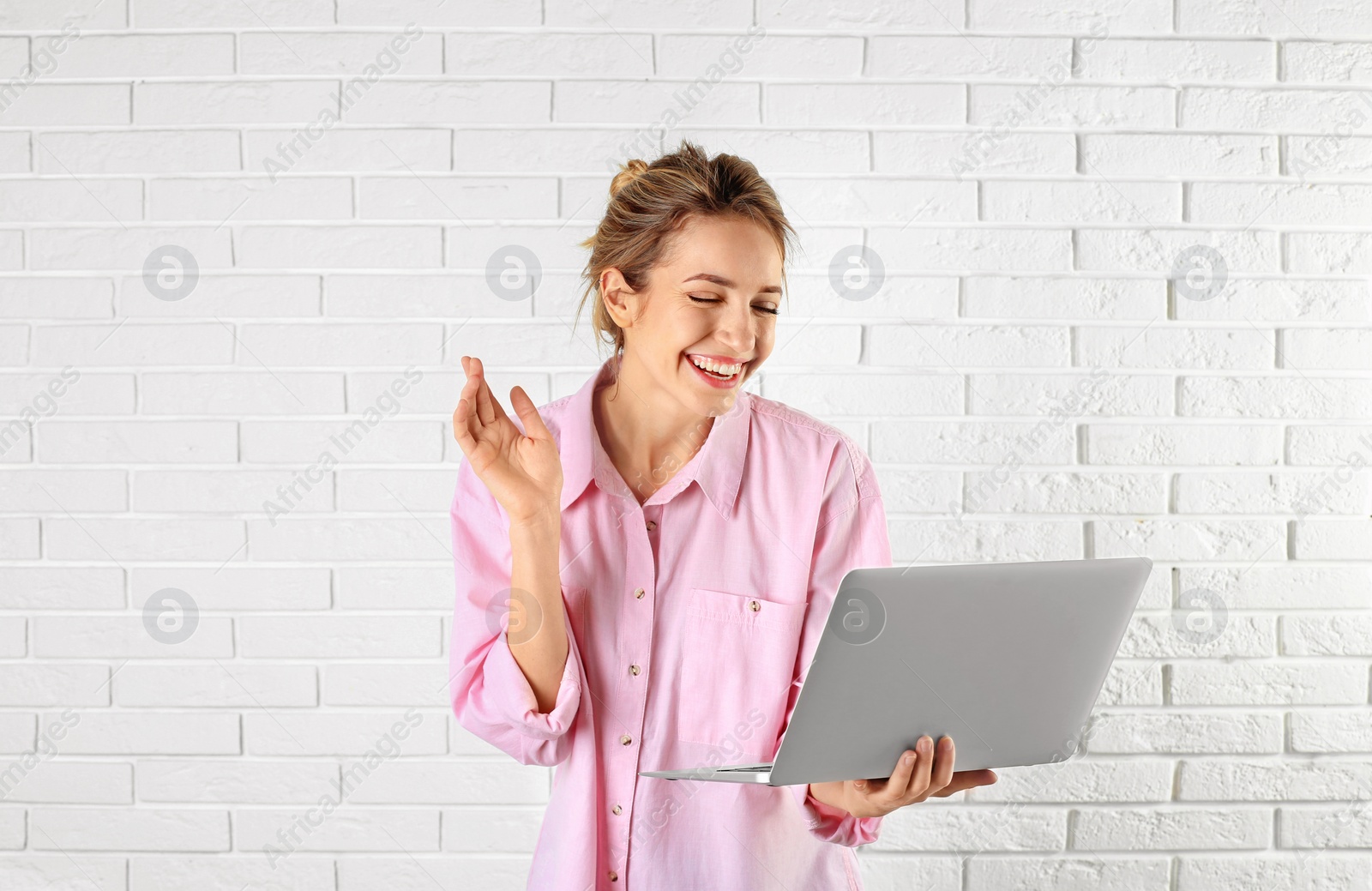 Photo of Woman using laptop for video chat against brick wall