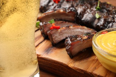 Photo of Glass of beer, tasty grilled ribs and sauce on wooden table, closeup