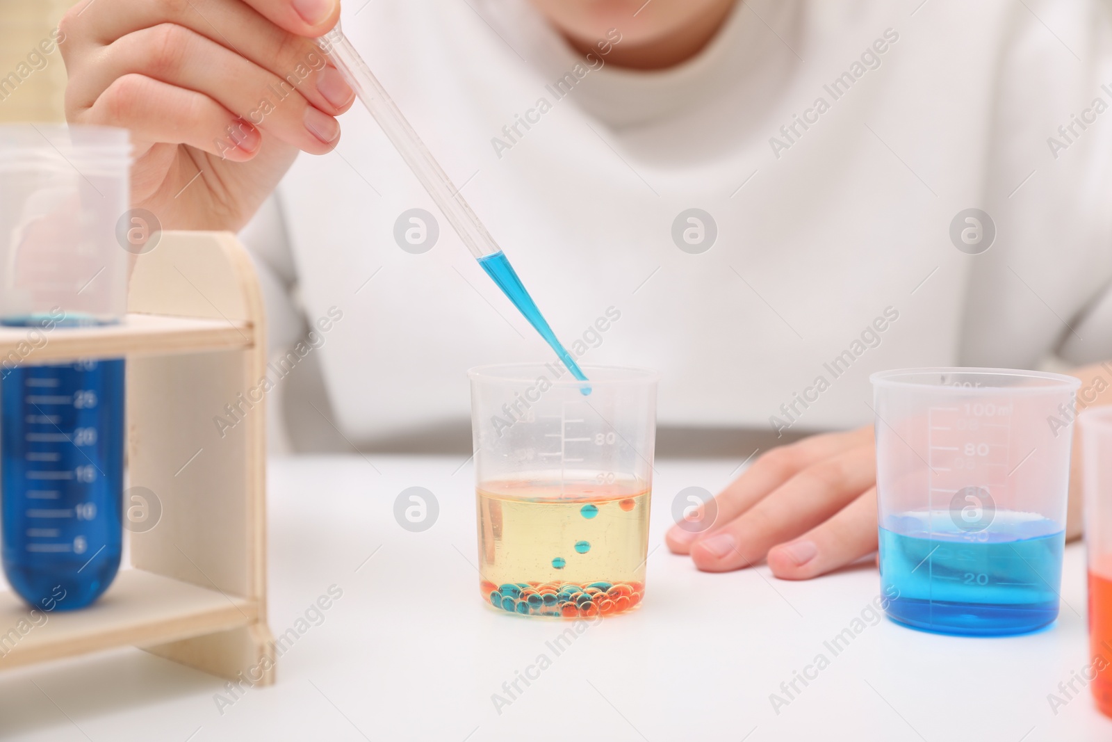 Photo of Girl mixing colorful liquids at white table indoors, closeup. Chemical experiment set for kids