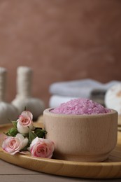Photo of Bowl of pink sea salt and roses on wooden table, closeup. Space for text