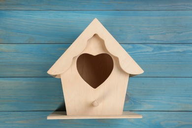 Photo of Beautiful bird house with heart shaped hole on light blue wooden background