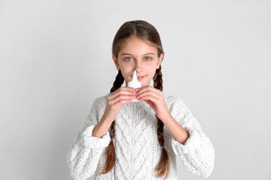 Photo of Sick little girl using nasal spray on white background