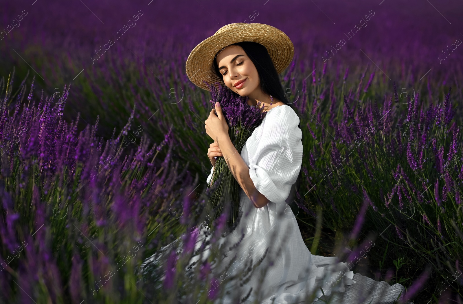 Photo of Beautiful young woman with bouquet sitting in lavender field