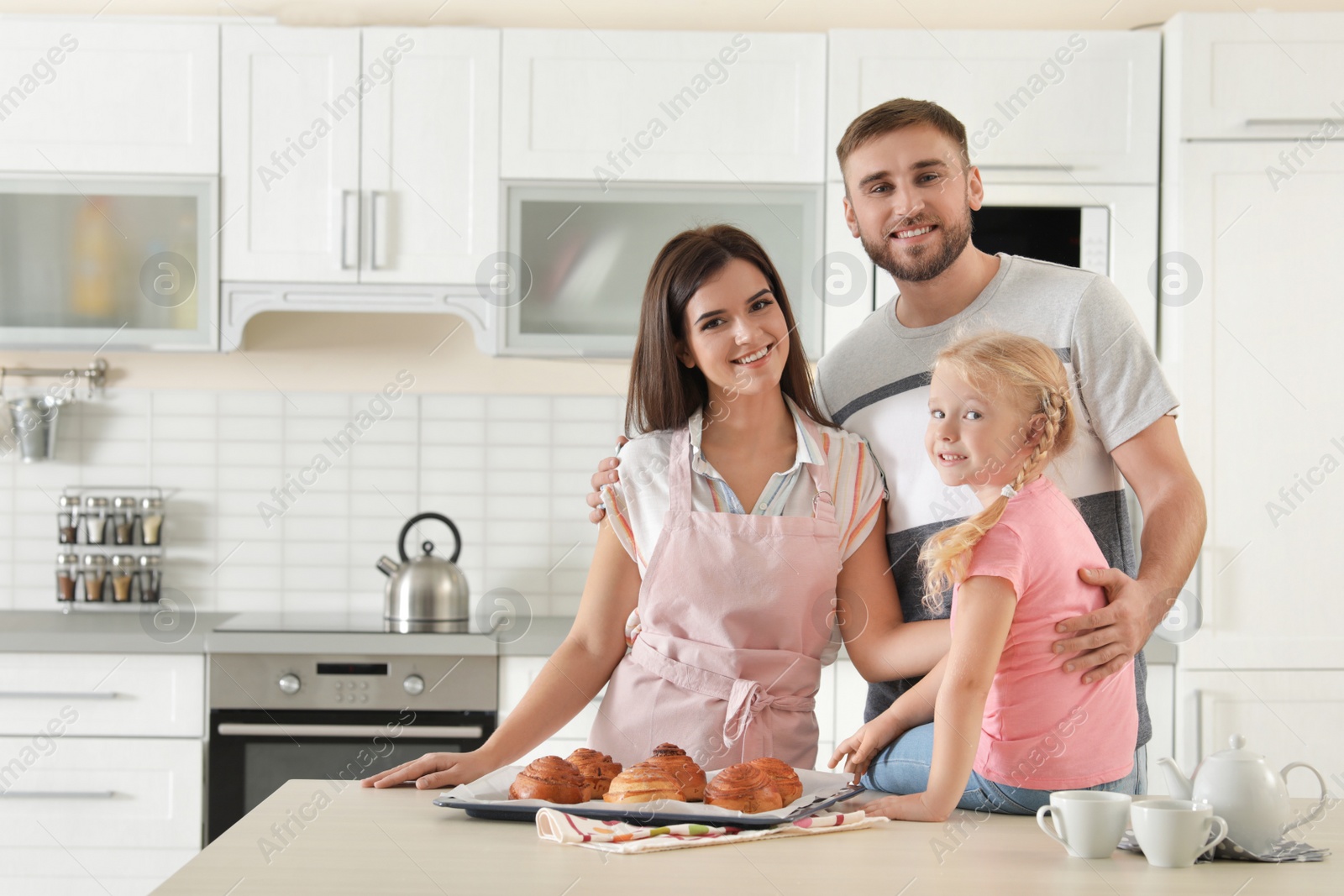 Photo of Happy family with tray of freshly oven baked buns at table in kitchen. Space for text