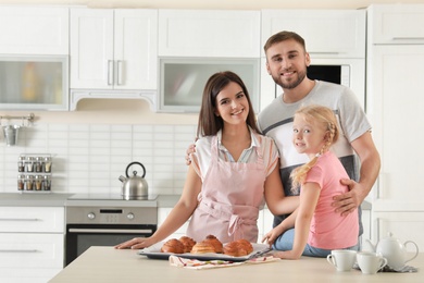 Happy family with tray of freshly oven baked buns at table in kitchen. Space for text