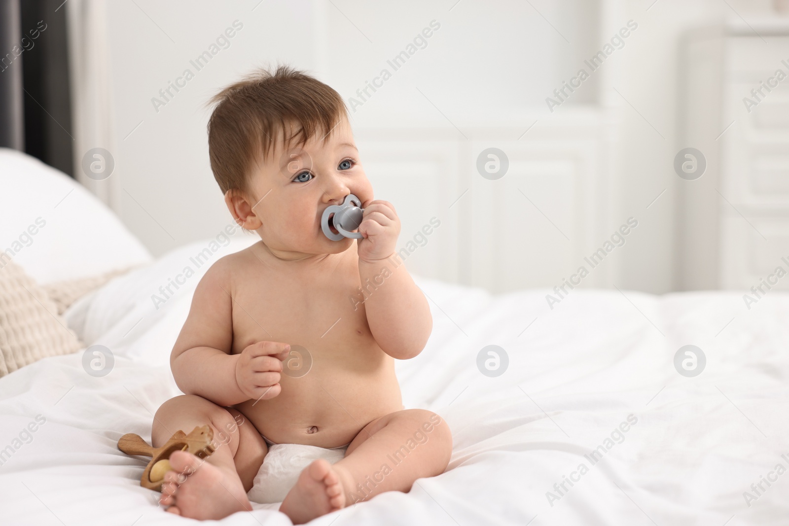 Photo of Cute baby boy with pacifier and wooden rattle on bed at home. Space for text