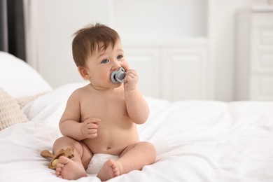 Cute baby boy with pacifier and wooden rattle on bed at home. Space for text