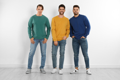 Group of young men in stylish jeans near white wall