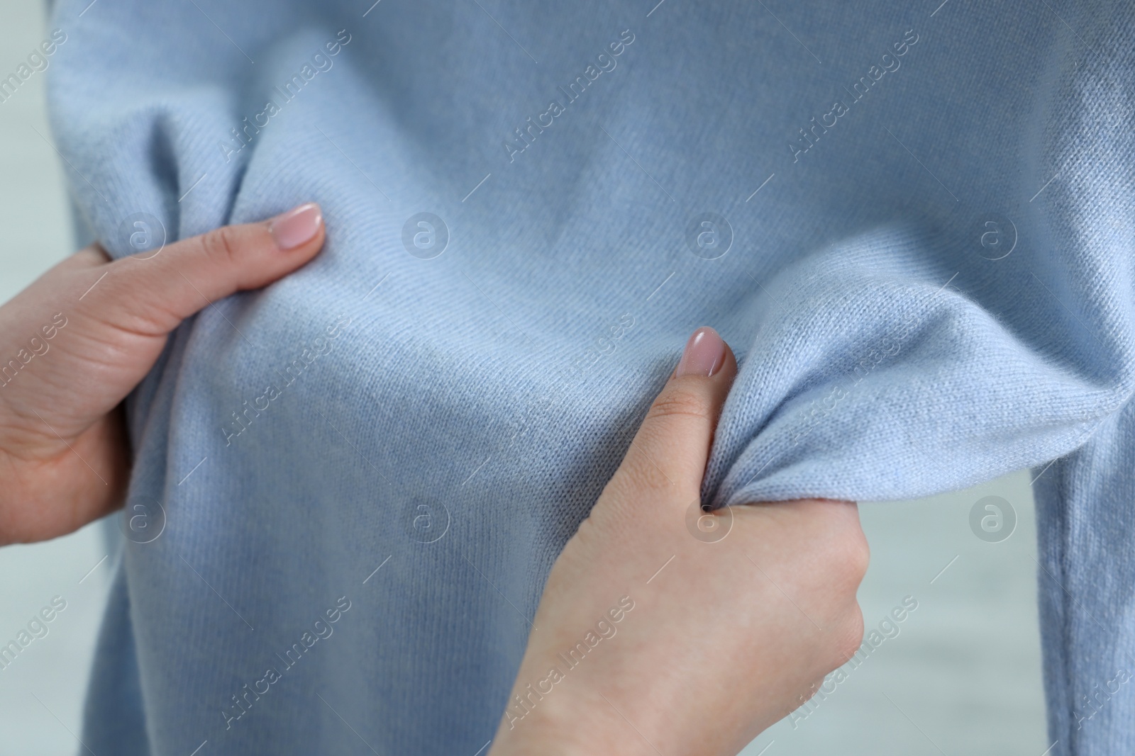 Photo of Woman touching clothes made of soft light blue fabric indoors, closeup