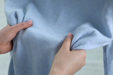 Photo of Woman touching clothes made of soft light blue fabric indoors, closeup