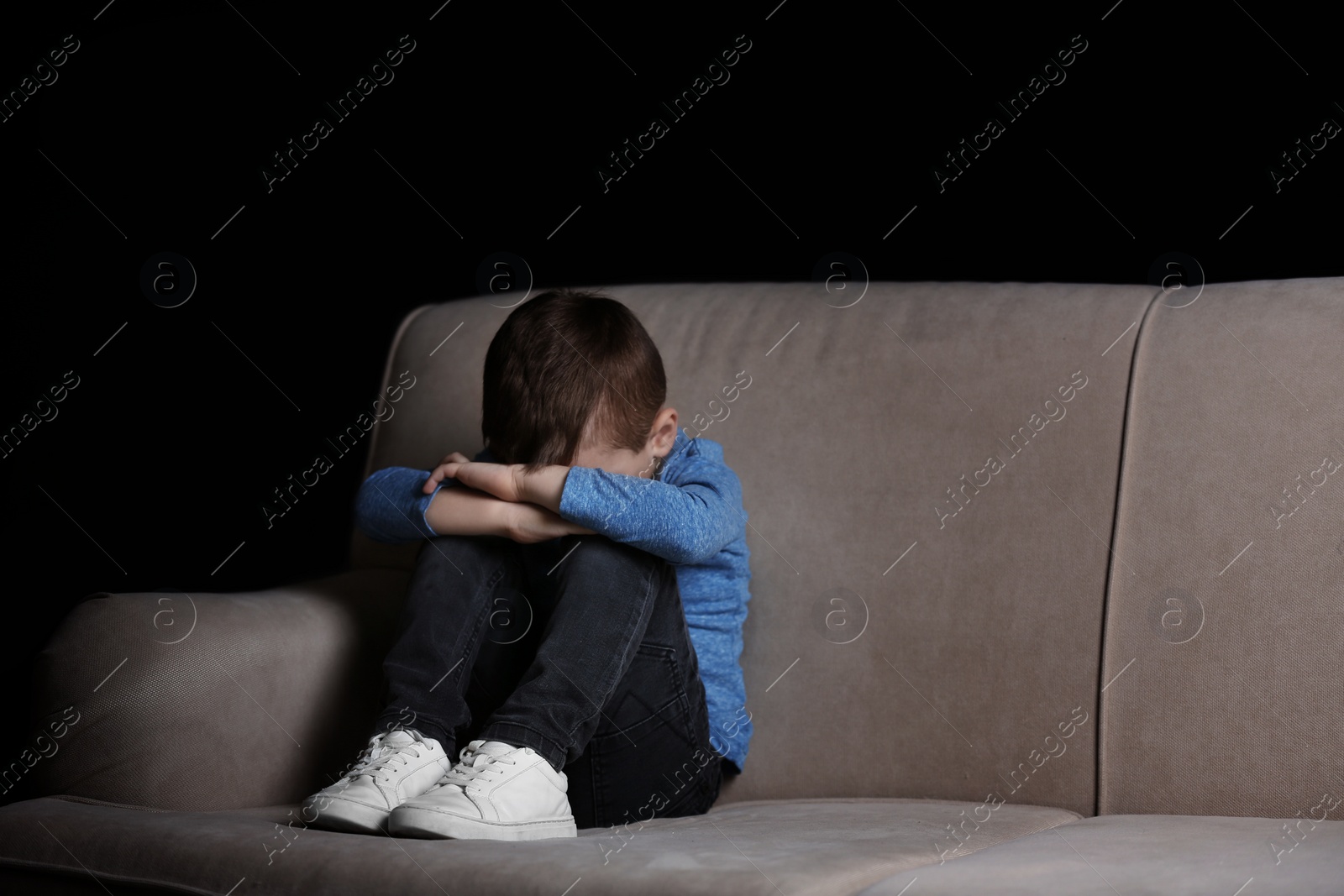 Photo of Sad little boy sitting on couch at home, space for text