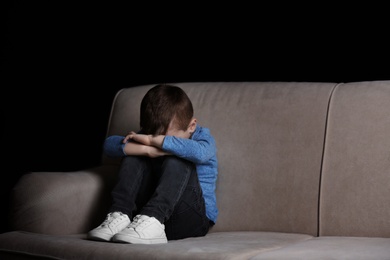 Photo of Sad little boy sitting on couch at home, space for text