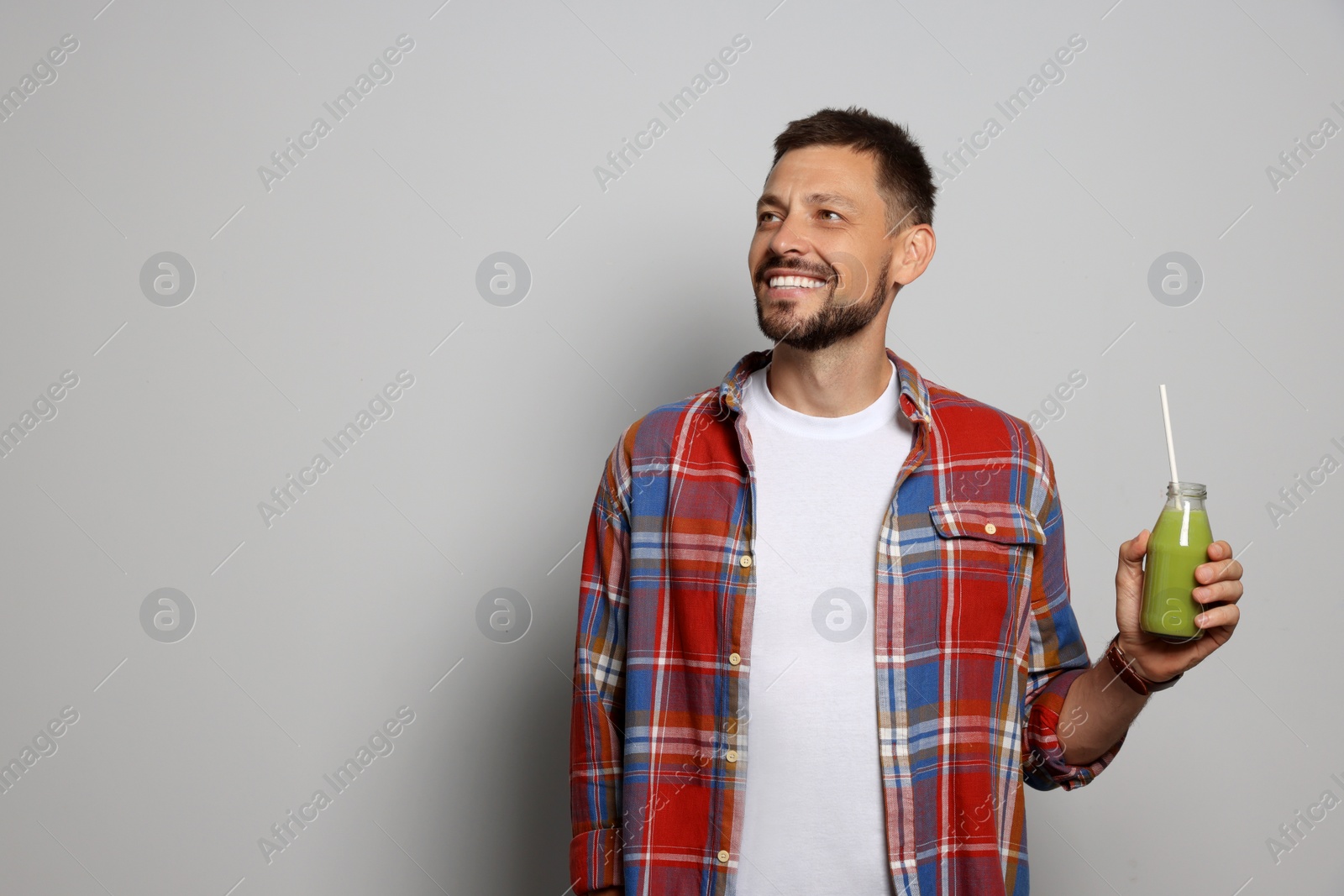 Photo of Happy man holding bottle of delicious juice on grey background, space for text