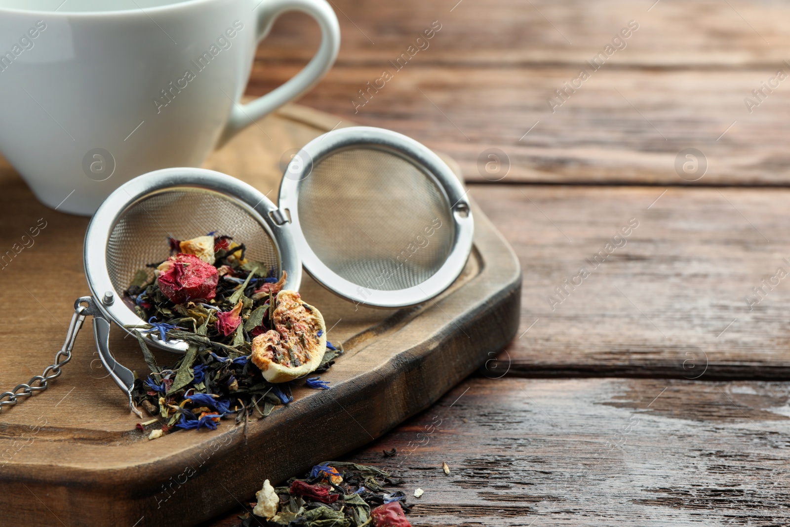 Photo of Snap infuser with dried herbal tea leaves and fruits on wooden table, closeup. Space for text