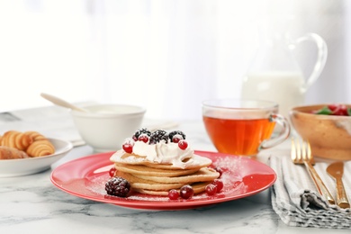 Photo of Delicious pancakes with berries and cream served for breakfast on table