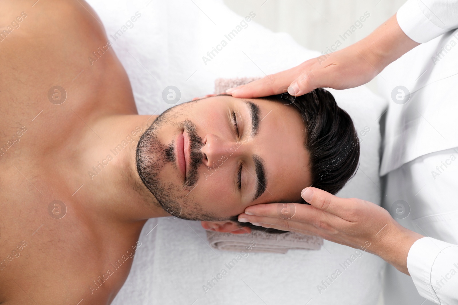 Photo of Handsome young man receiving face massage on spa table, top view