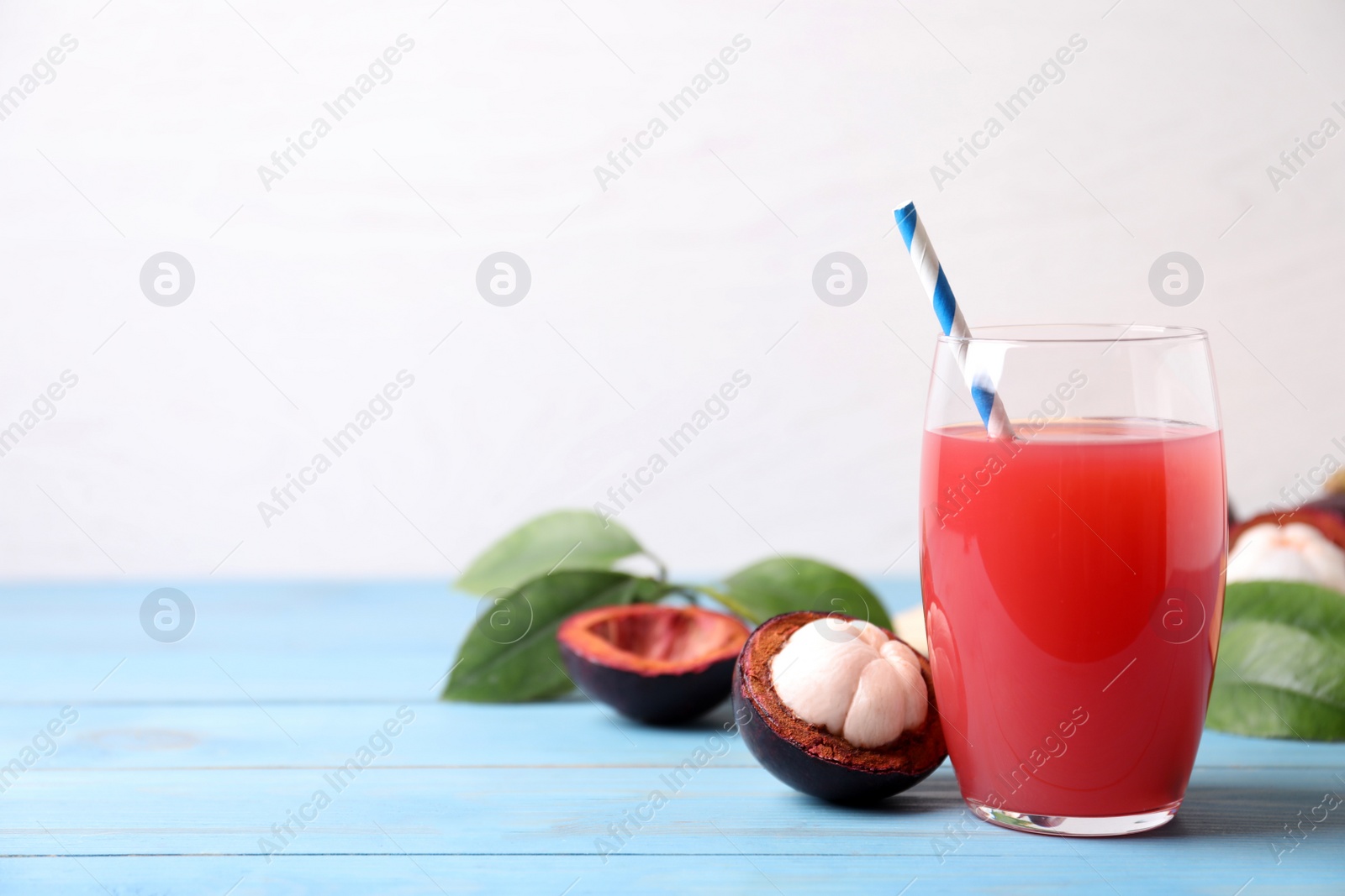 Photo of Delicious fresh mangosteen juice in glass on light blue wooden table, space for text