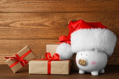 Piggy bank with Santa hat and gift boxes on wooden table