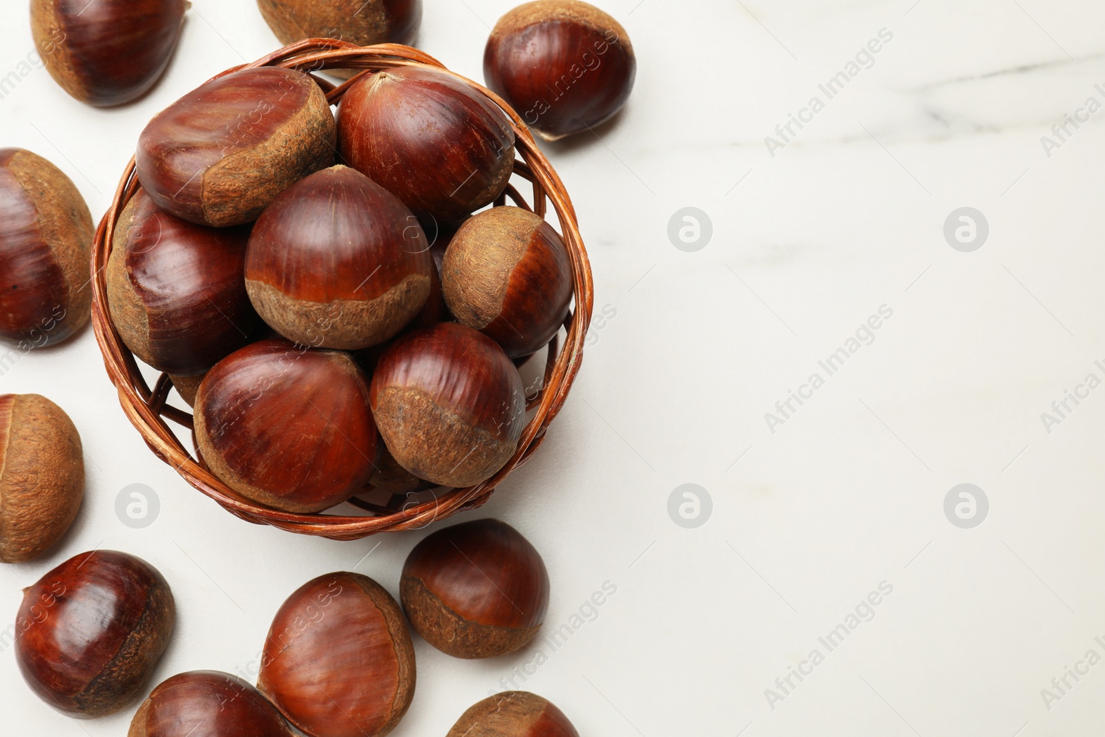 Photo of Sweet fresh edible chestnuts in wicker bowl on white marble table, top view. Space for text