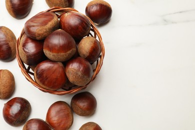 Photo of Sweet fresh edible chestnuts in wicker bowl on white marble table, top view. Space for text