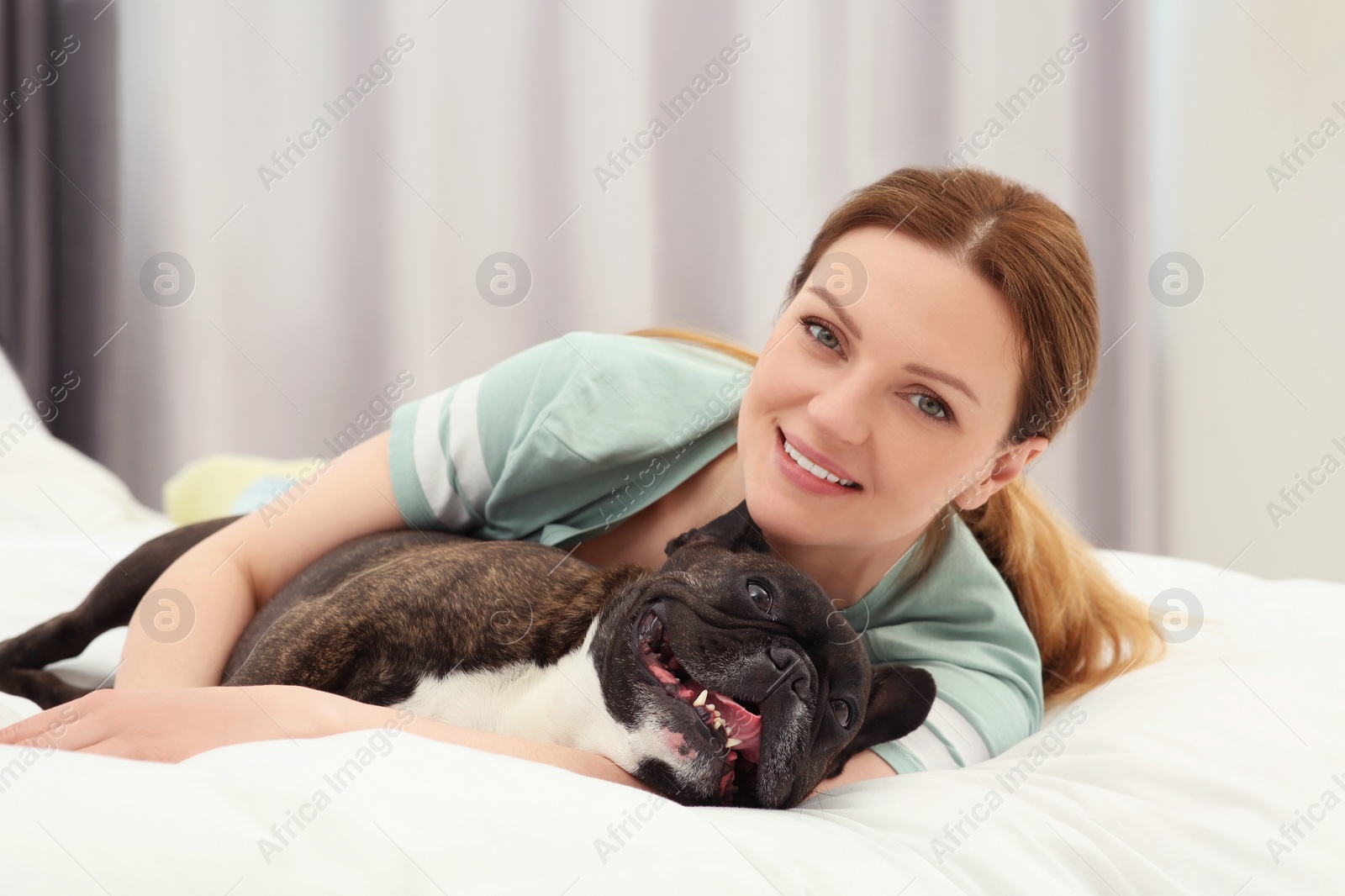 Photo of Happy woman hugging with cute French Bulldog on bed in room