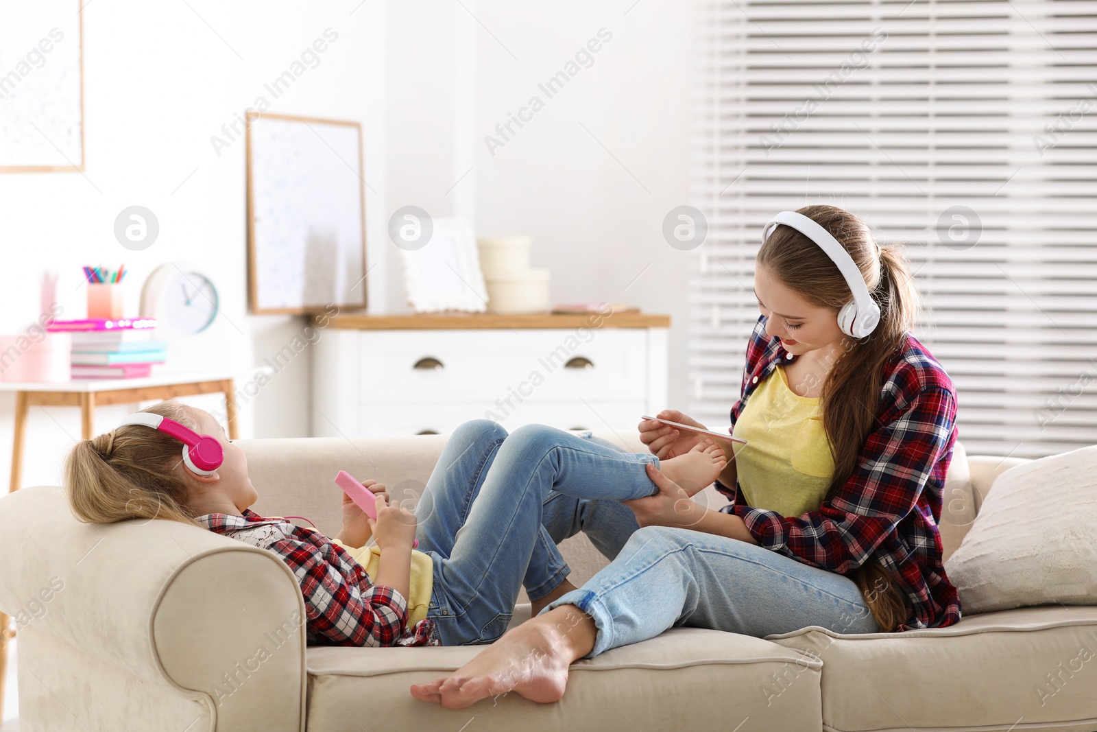 Photo of Happy mother and little daughter with headphones filing nails on sofa at home