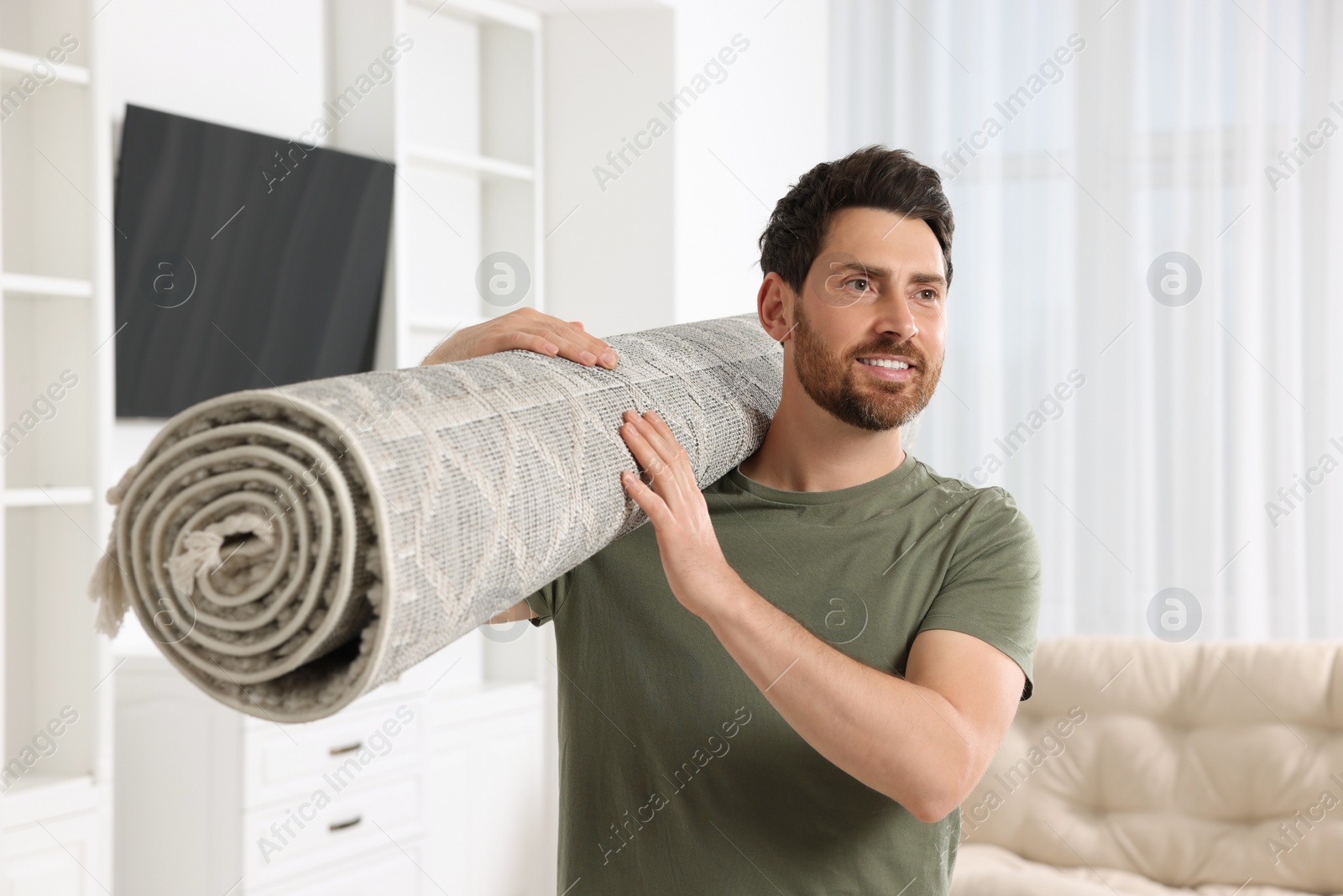 Photo of Smiling man holding rolled carpet in room