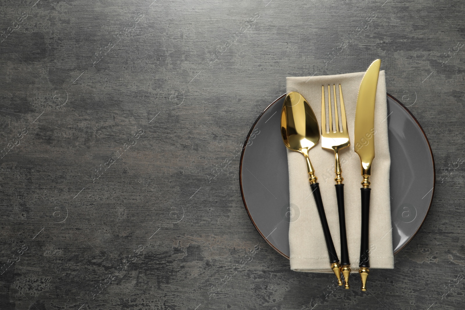 Photo of Elegant setting with golden cutlery on dark grey table, top view. Space for text