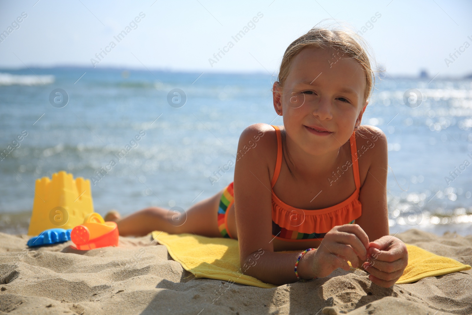 Photo of Little girl playing with sand on beach near sea, space for text