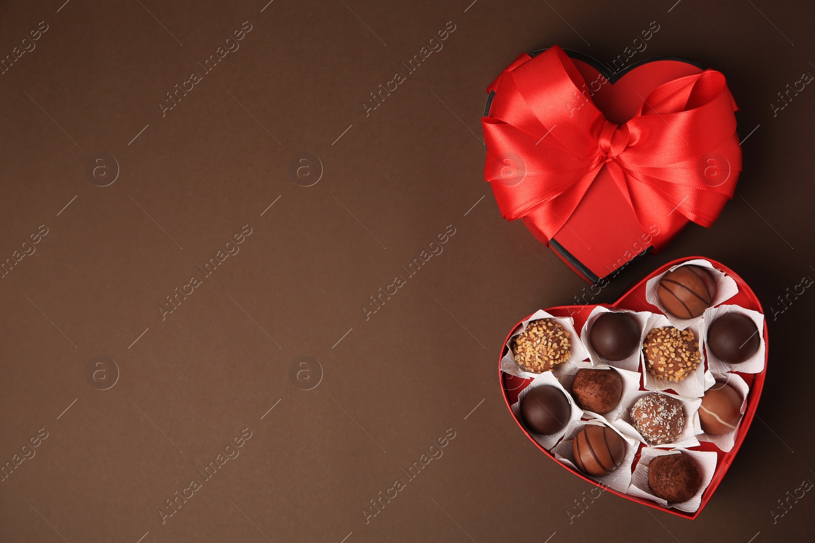 Photo of Heart shaped box with delicious chocolate candies on brown background, flat lay. Space for text